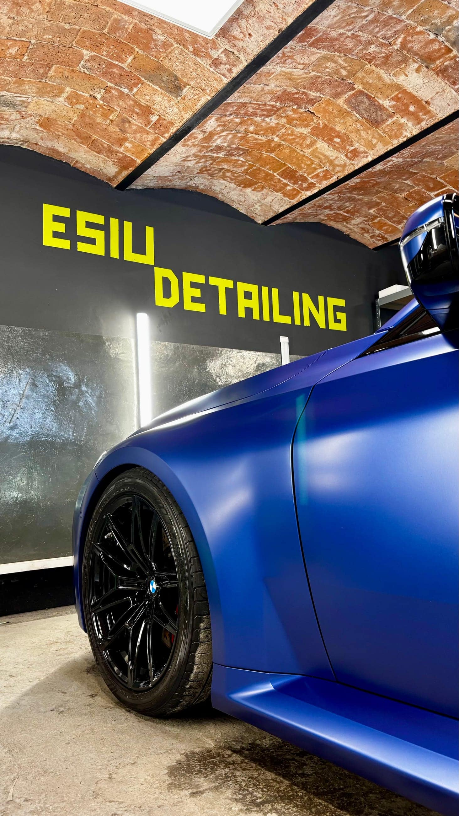 Matowe BMW M2 G87 pod żółtym szyldem ESIU Detailing i ceglanym sklepieniem studia w Batowicach